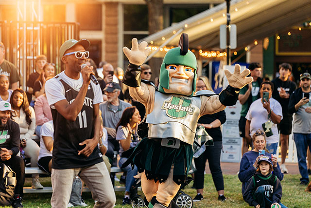 a person with a microphone and Sparty, the USC Upstate mascot