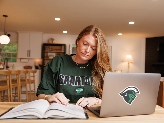 USC Upstate student sits at a table with her laptop and textbook