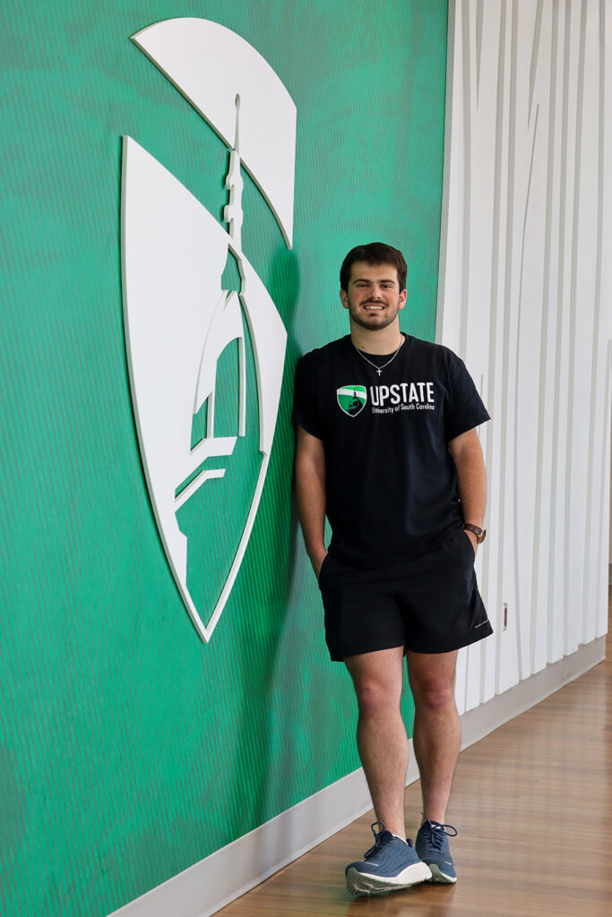 Pierre Laurent-Courrier poses beside a green wall with the Upstate dome logo
