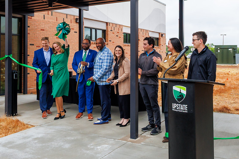 A group of people cheer as they cut the ribbon to a new Health Services building
