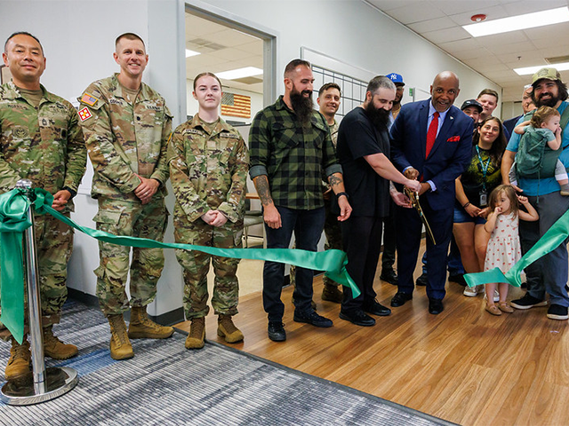 People cut a green ribbon for the grand opening of a new veterans lounge.