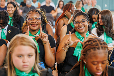 two students in a crowd gesture a U sign with their hands